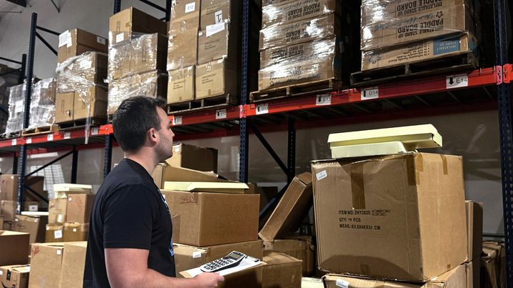 A Rudderr team member checking inventory between warehouse shelves stacked with cartons